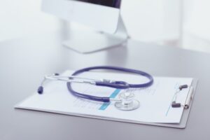 A stethoscope and a patient chart lying on top of a metallic desk