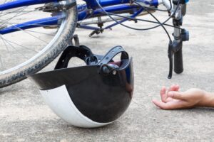 A close up image of a childs cycle helmet on the ground with a bicycle. 