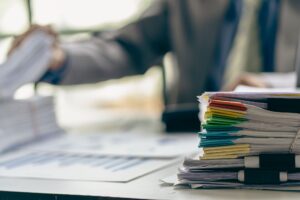 A desk contains paperwork with a person in the background working on a claim for fractured sternum compensation. 