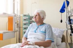 An elderly patient sits on a hospital bed.