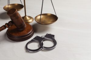 A pair of handcuffs, a gavel, and justice scales on a plain cream table. 