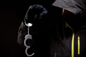 A dark hooded silhouette figure holding a pair of handcuffs. 