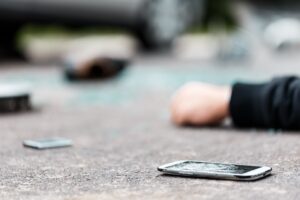 A pedestrian and a broken phone lay in the road. 