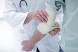 An NHS staff injury being treated by a doctor who is wrapping a bandage around someone's elbow.