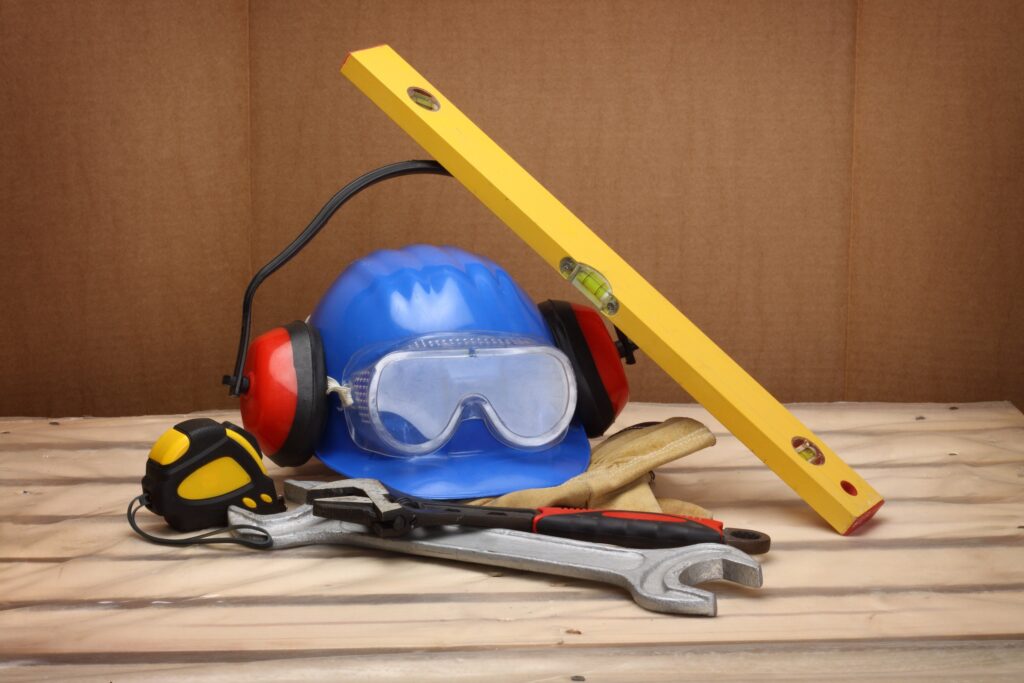 Safety equipment such as a hard hat and safety goggles lying on some wood.