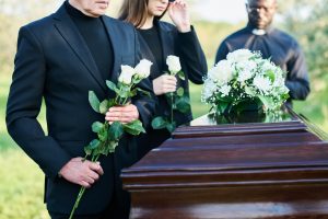 A coffin at a funeral with famly members placing white flowers on top.