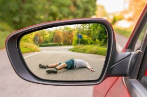 A man lying in the middle of the road views from a side-view mirror on a car