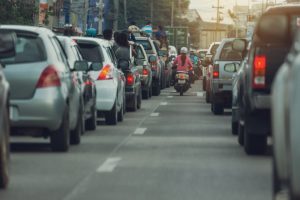 Motorcycle driving on road between two queues of cars.