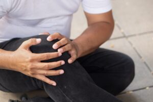 A person sits on the ground holding their knee.