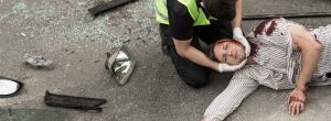 A man with a serious injury with blood on his head laying on his back next to a member of emergency services.